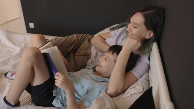 A mother and her son share a special moment as they read a book together in bed. This heartwarming scene captures the love and connection between parent and child.
