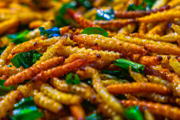 A vivid close-up of crispy fried worms mixed with green herbs, showcasing golden textures and vibrant contrast—highlighting Thai street food's bold protein-rich culinary heritage.