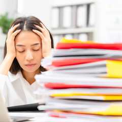 Exhausted Chinese woman struggles with overwhelming pile of documents in busy office environment