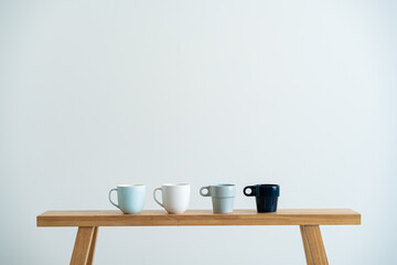 Minimalist cups on a wooden bench against white wall
