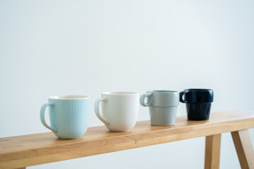 Minimalist cups on a wooden bench against white wall