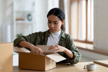 Woman unpacking cardboard box at home after online shopping delivery order arrival