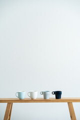 Minimalist cups on a wooden bench against white wall