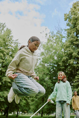 Multiethnic group of children playing jump rope outdoors in park, preteen girl with dark hair...