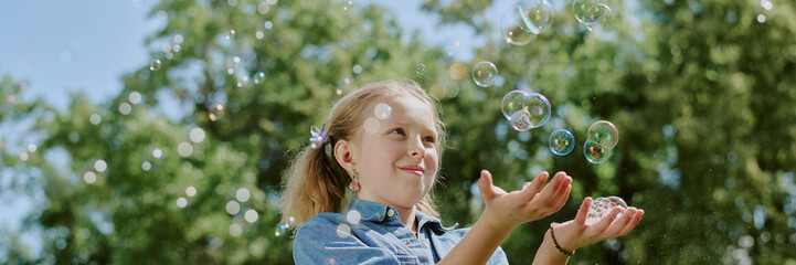 Caucasian girl child smiling and playing with soap bubbles outdoors in park, holding hands up and...
