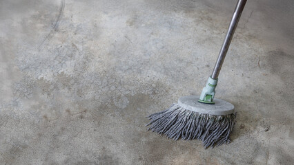 Close-up image of a round mop head cleaning an old, stained concrete floor. The image shows cleaning in progress, with visible texture and cracks on the floor surface