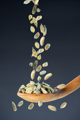 Whole cardamom seeds fall from above onto a wooden spoon, ideal for aromatic seasoning and exotic...