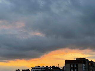 Dramatic sunset sky with orange hues and dark clouds over a city silhouette.