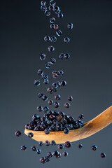 Fresh dried juniper fall from above onto a wooden spoon, ideal for culinary herbs and aromatic...