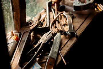 On the old wooden table lie tools: hammers, screwdrivers, wrenches, next to them is a tube of glue and metal parts.