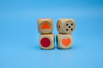 Four wooden dice with vibrant colors and simple shapes colored circles, a diamond shape, and number dots placed in a row on a light blue background. Suitable for education, preschool activities
