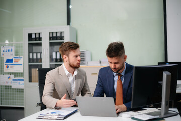Professional businessmen collaborating in modern office, using laptop and tablet, discussing strategy, teamwork, and innovation.