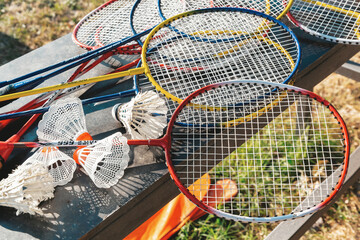 Colorful badminton rackets and shuttlecocks on outdoor table in sunlight during summer leisure activity