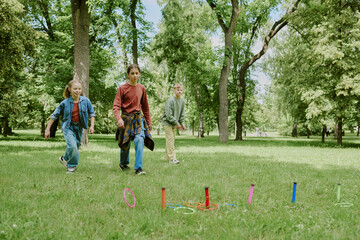 Fototapeta premium Group of Caucasian children walking on grass with female school teacher supervising in park, kids participating in outdoor activity together surrounded by green trees
