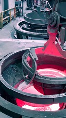 A close-up view inside a metal foundry where glowing red molten metal is being processed inside a large industrial machine, highlighting the extreme heat and powerful machinery.