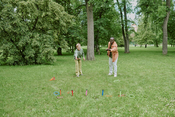 Caucasian boy and Black man playing ring toss game together in green park, teacher guiding child...