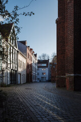 A narrow cobblestone street curves through a historic district of Bremen, Germany, flanked by traditional European buildings with varied facades.