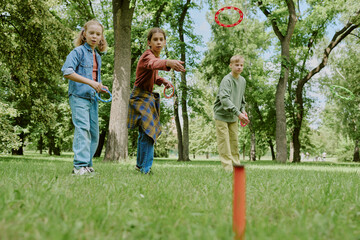 Group of Caucasian children playing ring toss game in park, standing on grass and focusing on...