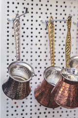 Closeup of traditional copper Turkish cezves with engraved brass handles hanging in street market display in Turkey