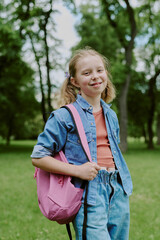 Portrait of Caucasian girl child smiling outdoors in park carrying backpack standing with trees in background representing student or pupil during school field trip