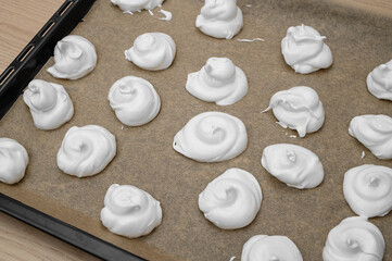 A baking tray lined with baking paper and white meringues made from egg whites on it