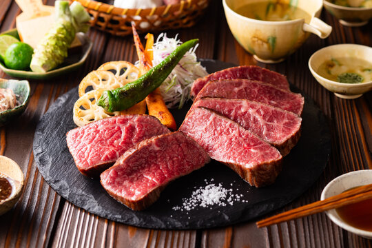 【黒毛和牛ステーキ】レアで美しく焼き上げた黒毛和牛モモ肉のステーキ。ジューシーな肉の旨みを引き立てるのは、素揚げした季節の野菜と彩り豊かな薬味。わさびや塩、日本酒とともに、和の美味を贅沢に味わう一皿です。