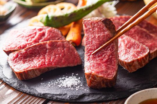【黒毛和牛ステーキ】レアで美しく焼き上げた黒毛和牛モモ肉のステーキ。ジューシーな肉の旨みを引き立てるのは、素揚げした季節の野菜と彩り豊かな薬味。わさびや塩、日本酒とともに、和の美味を贅沢に味わう一皿です。