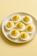 Traditional deviled eggs served on a white plate with pastel yellow background &mdash; classic American appetizer with creamy yolk filling, minimalist food presentation
