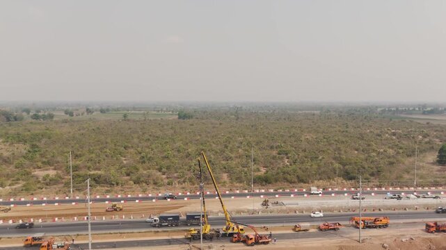 Drone footage aerial view scenic landscape Cranes and mechanics repair high-voltage power lines along a rural road under construction
