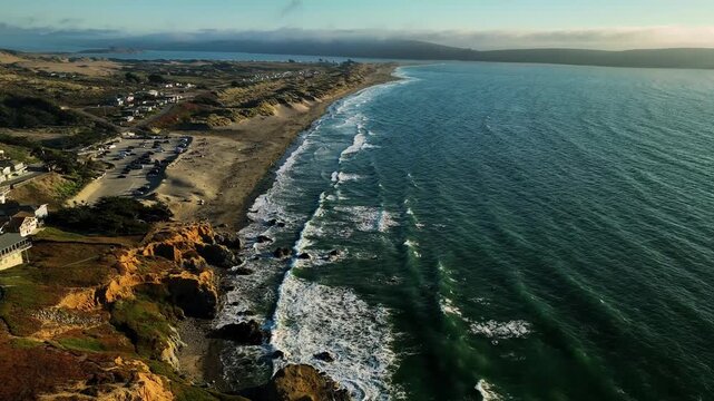 Aerial view of the Pacific Ocean's turquoise waters meeting the sandy shore and rugged cliffs of Point Reyes, California, United States.