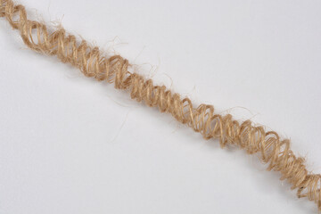 This diagonal, extreme close-up studio shot captures a single strand of natural jute twine coiled...