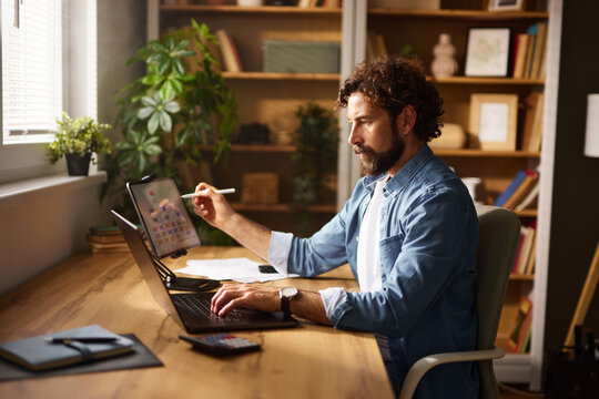 An individual is engaged in work at a home office, utilizing a laptop and tablet to complete tasks.