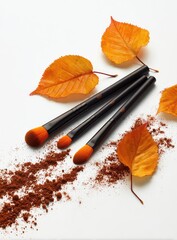 Three black makeup brushes, autumnal leaves, and scattered brown powder