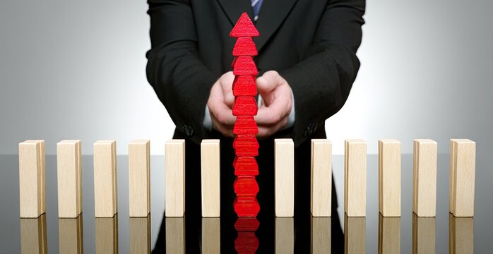 Businessperson builds a red upward-pointing stack of wooden blocks while other wooden blocks line the image