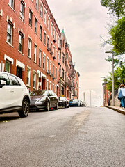 Steep residential street lined with red brick buildings and parked cars