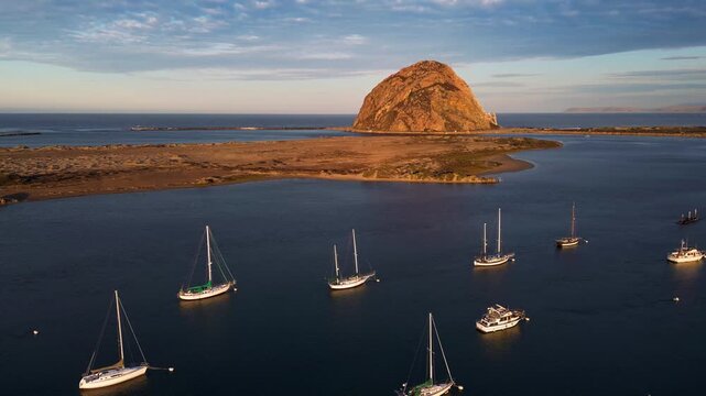 Aerial view of boats in the bay with the majestic Morro Rock standing tall against a serene sky, Morro Bay, California, United States.