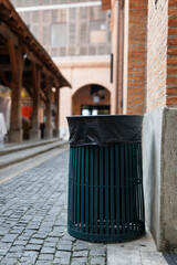 Public trash can standing on cobblestone street in a market