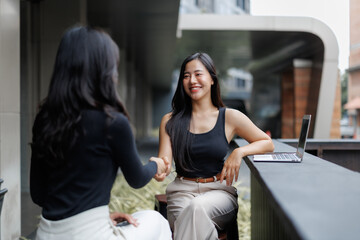 Two businesswomen shaking hands in a modern city setting