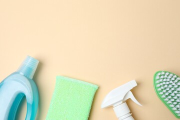Flat lay of various cleaning supplies forming a bottom border on a pactel beige background. Includes brush, sponge, spray bottle, detergent. Housekeeping concept with copy space.