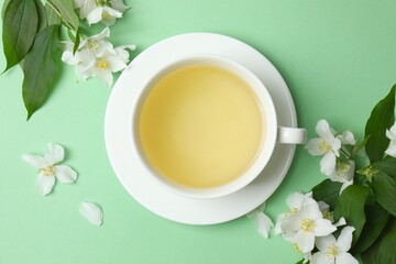 Cup of hot tea with jasmine flowers on green background, close up