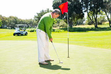 Senior African American man putting ball with putter on golf green next to flagstick, copy space