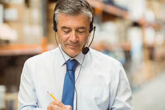 Middle-aged man surveying warehouse aisle wearing shirt and tie with headset and clipboard