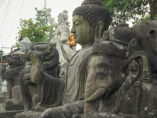 Rows of Buddha and Hindu deity statues, including Ganesha, sit outdoors in a stone carving shop....