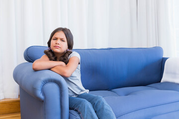 Obraz premium School-aged girl leaning on blue sofa arm in living room with white drapes, copy space