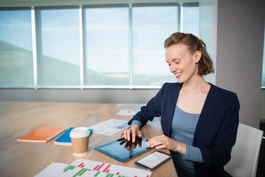 Business professional tapping tablet at wooden meeting table with graphs, smartphone and hills view - Powered by Adobe