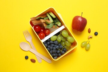 The lunchbox features delectable sandwiches and fresh snacks on a yellow background. A school lunch concept