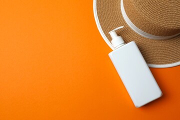 White sunscreen bottle on orange surface with straw hat conveying summer vibes, space for text