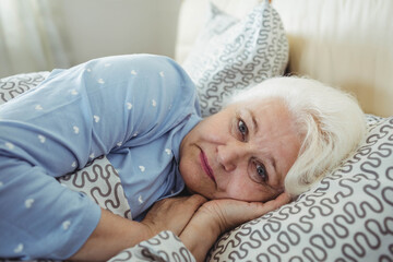Senior woman wearing heart patterned pajamas lying in bed resting head on pillow