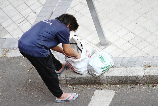 Pobre mendigo indigente con hambre buscando entre bolsas de basura en la acera de la calle