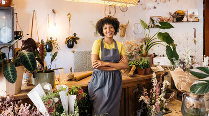 Florist owner smiling with crossed arms in her flower shop, surrounded by plants and flowers